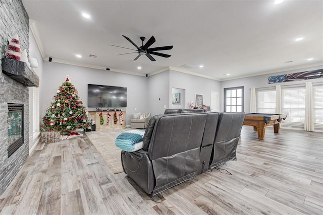 living room featuring ceiling fan, crown molding, light hardwood / wood-style flooring, billiards, and a stone fireplace