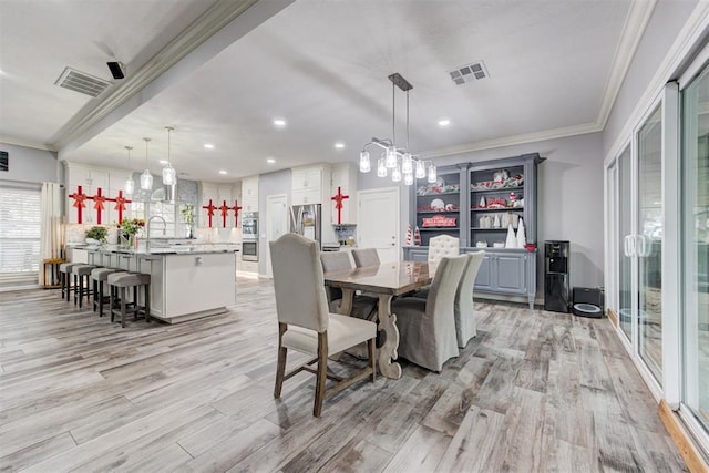 dining room with crown molding, sink, and light wood-type flooring