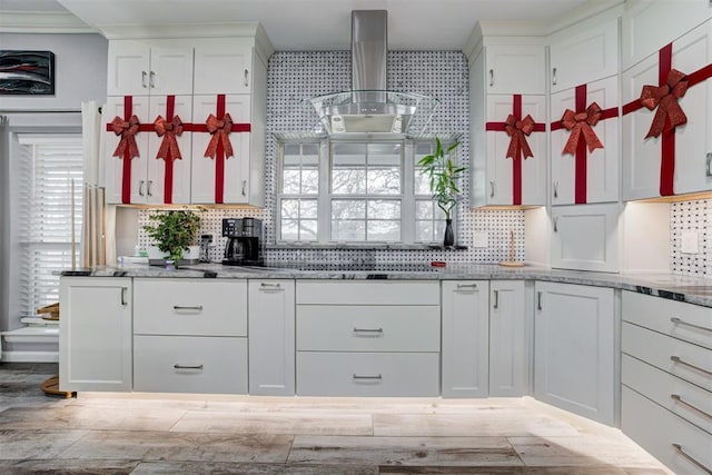 kitchen with backsplash, white cabinets, and wall chimney range hood