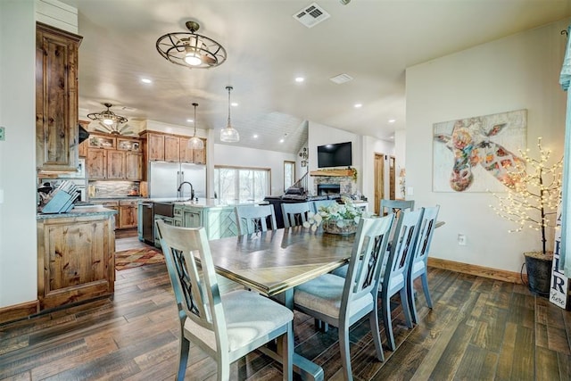 dining space featuring vaulted ceiling, dark hardwood / wood-style floors, a stone fireplace, and ceiling fan