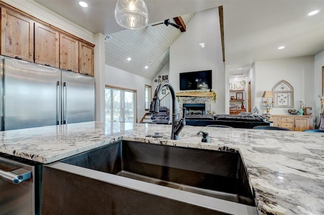 kitchen with light stone countertops, sink, pendant lighting, a fireplace, and lofted ceiling