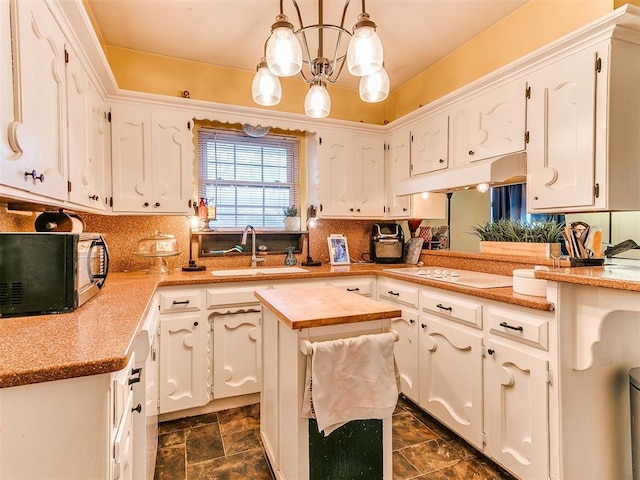 kitchen with decorative light fixtures, sink, white cabinets, and white stovetop