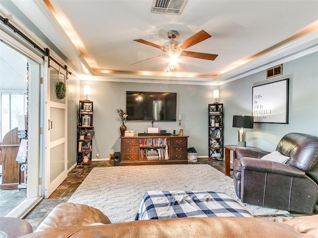 living room featuring ceiling fan, a barn door, ornamental molding, and a raised ceiling