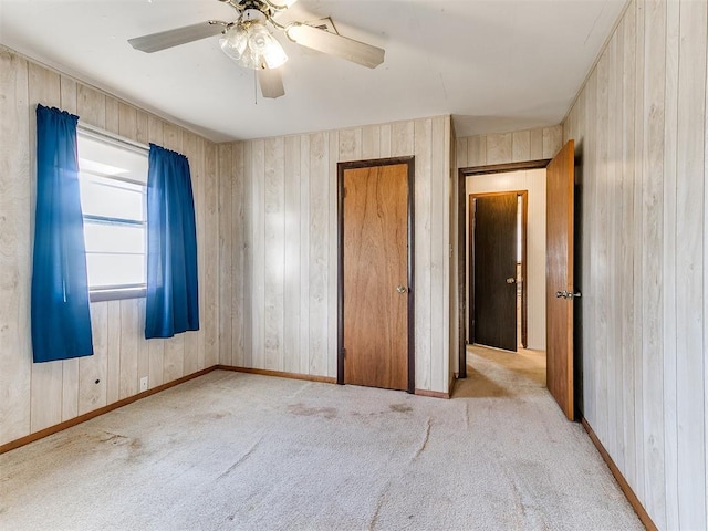 unfurnished bedroom featuring ceiling fan, light carpet, and wooden walls