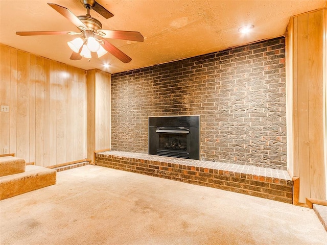 unfurnished living room with carpet flooring, wooden walls, ceiling fan, and a brick fireplace