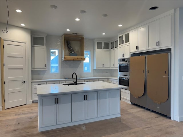 kitchen featuring white cabinetry, a kitchen island with sink, refrigerator, and double oven