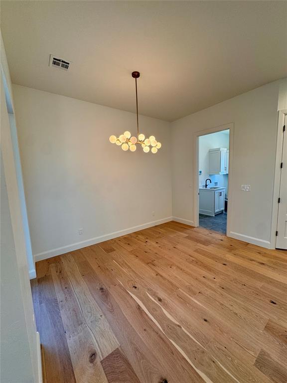 8409 NW 128th St, Oklahoma City, OK 73142 - empty room featuring a chandelier, light wood-style flooring, baseboards, and a sink