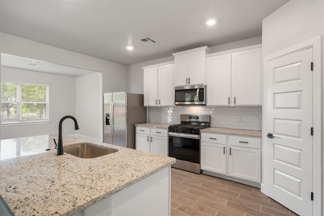 kitchen featuring white cabinets, stainless steel appliances, a center island with sink, and sink