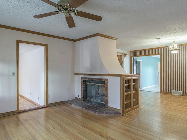 unfurnished living room with ceiling fan with notable chandelier, crown molding, a fireplace, a textured ceiling, and wood-type flooring