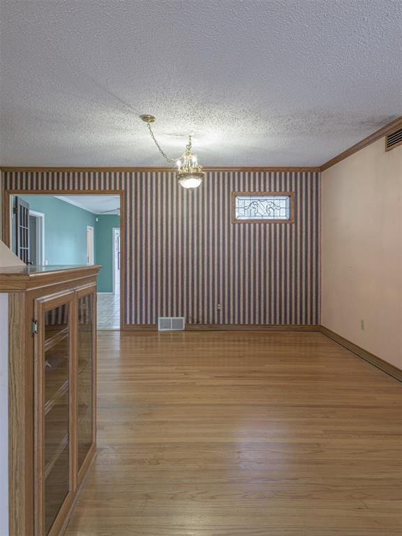 empty room featuring a textured ceiling, light hardwood / wood-style flooring, crown molding, and a notable chandelier