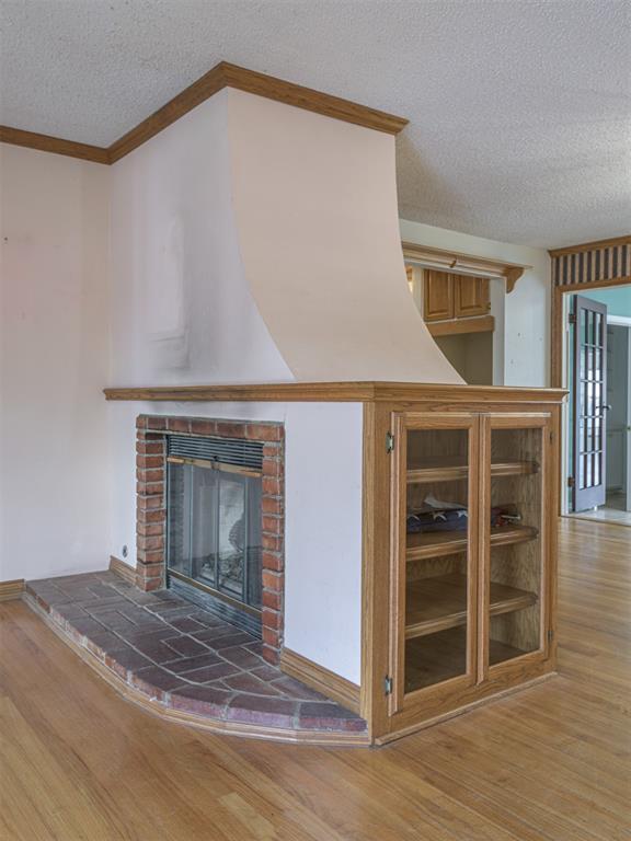 unfurnished living room with hardwood / wood-style floors, ornamental molding, a textured ceiling, and a brick fireplace