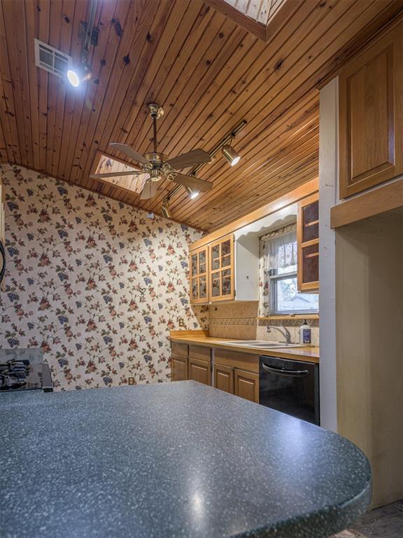 kitchen with a skylight, sink, black dishwasher, track lighting, and wood ceiling