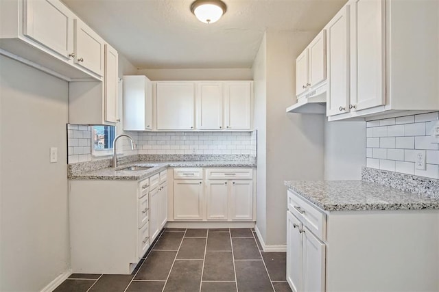 kitchen with dark tile patterned flooring, sink, decorative backsplash, light stone counters, and white cabinetry