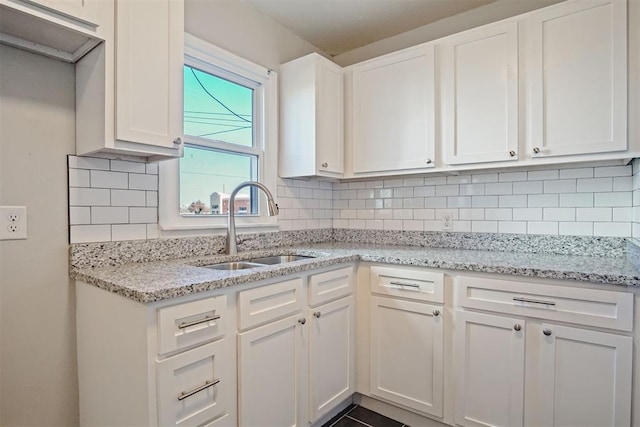 kitchen with decorative backsplash, light stone countertops, white cabinetry, and sink