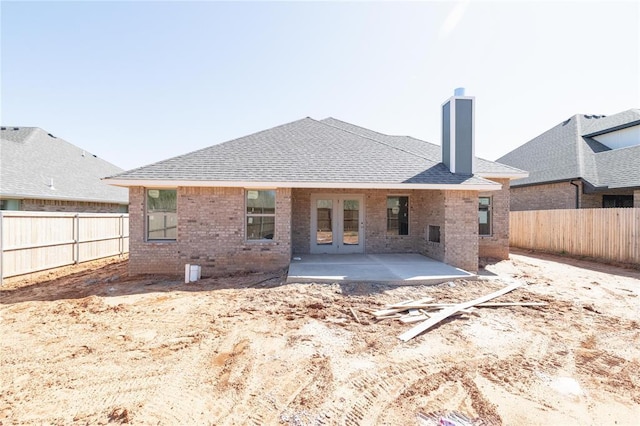 back of property featuring a chimney, french doors, a patio area, brick siding, and a fenced backyard