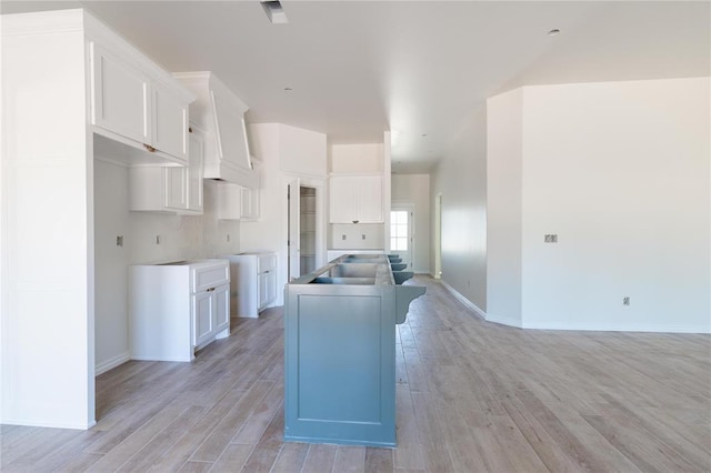 kitchen featuring light wood-style floors, a center island with sink, baseboards, and white cabinets