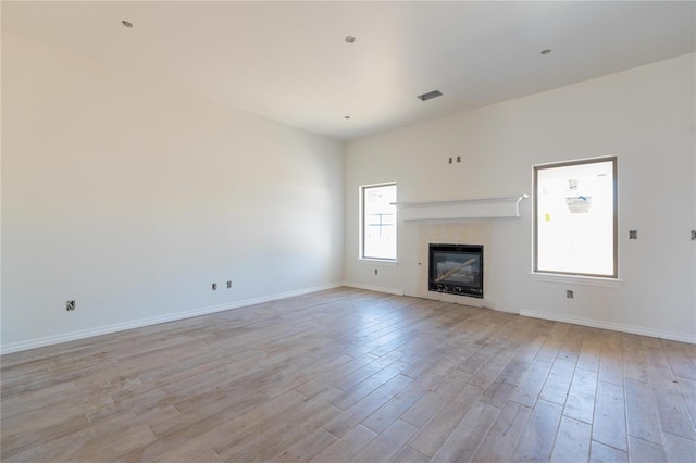 unfurnished living room featuring light wood-type flooring, baseboards, a glass covered fireplace, and visible vents