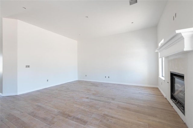 unfurnished living room with baseboards, light wood-type flooring, and a glass covered fireplace