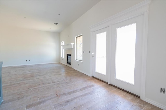unfurnished living room featuring visible vents, light wood-type flooring, a glass covered fireplace, and a healthy amount of sunlight