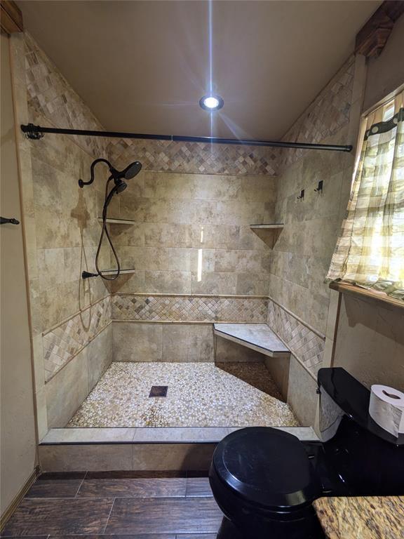 bathroom featuring hardwood / wood-style flooring, toilet, and tiled shower