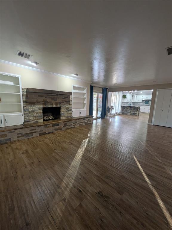 unfurnished living room with dark hardwood / wood-style flooring, a stone fireplace, ornamental molding, and built in shelves