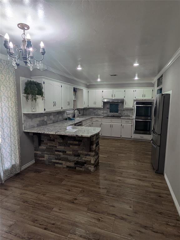 kitchen with an inviting chandelier, hanging light fixtures, dark hardwood / wood-style floors, kitchen peninsula, and stainless steel appliances