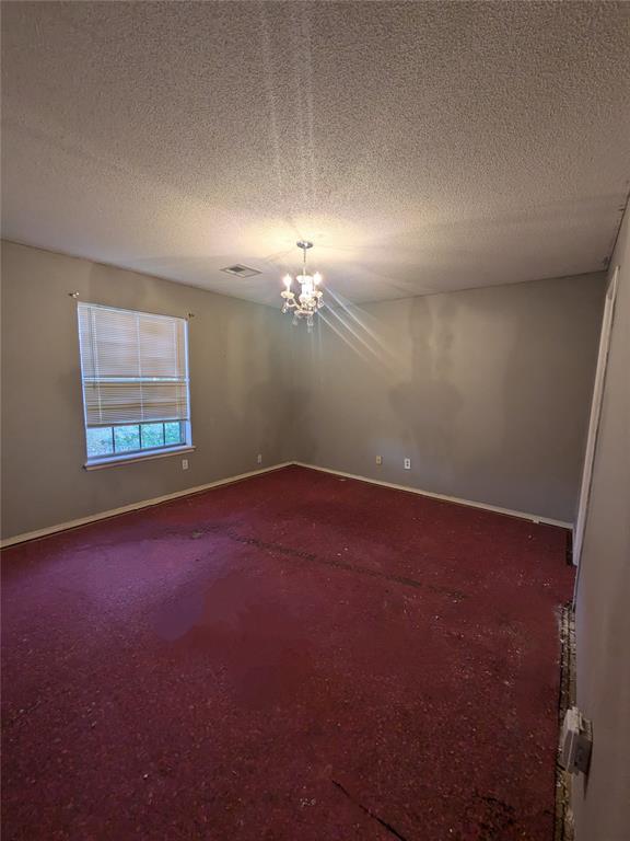 empty room featuring a textured ceiling, carpet floors, and an inviting chandelier