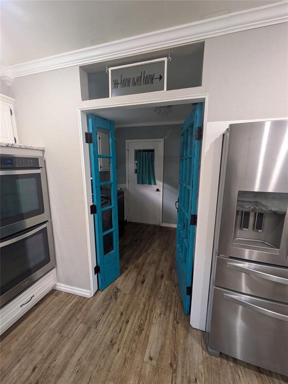 kitchen with white cabinets, ornamental molding, stainless steel appliances, and dark wood-type flooring