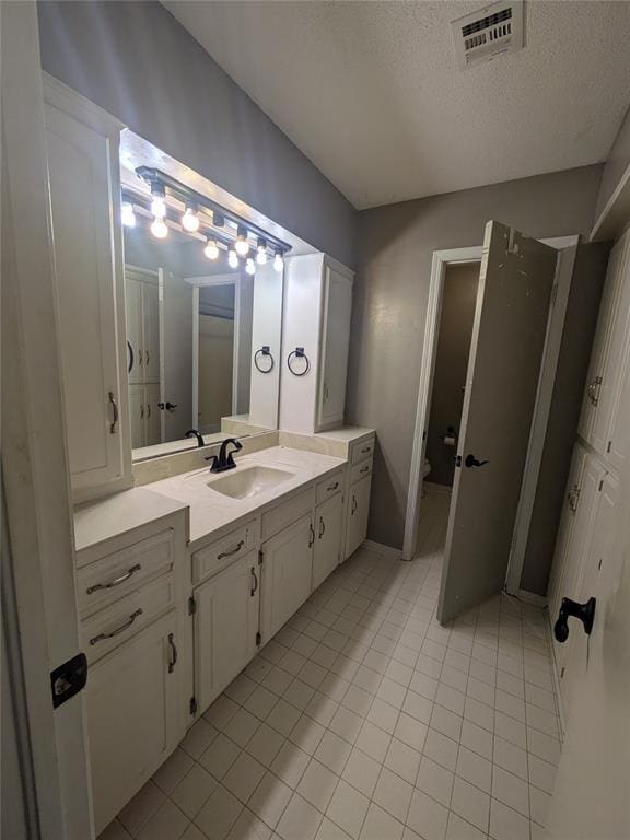 bathroom featuring tile patterned flooring, vanity, toilet, and a textured ceiling