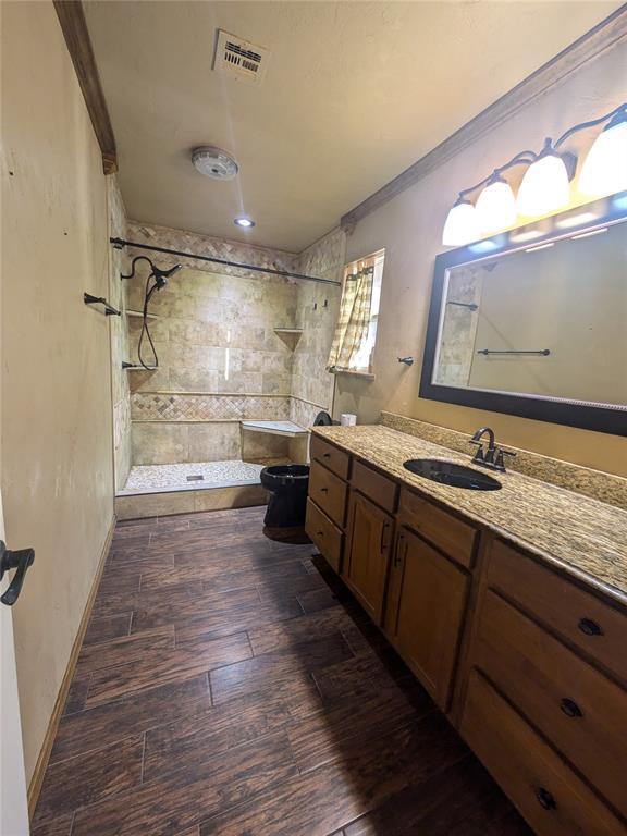 bathroom with a tile shower, vanity, wood-type flooring, and ornamental molding