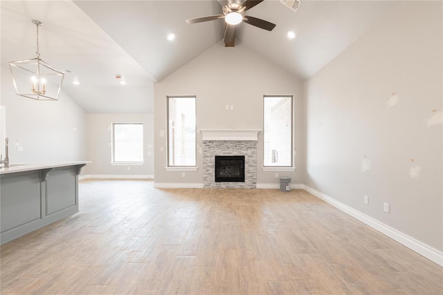 unfurnished living room with a fireplace, light wood-type flooring, beam ceiling, baseboards, and ceiling fan with notable chandelier