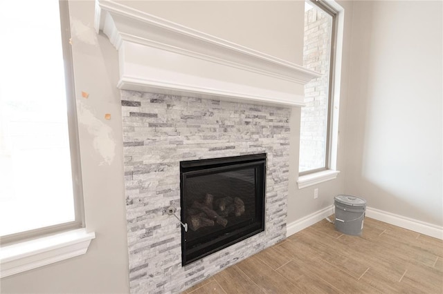 room details featuring baseboards, a stone fireplace, and wood finished floors