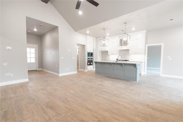 unfurnished living room with ceiling fan, a sink, light wood-style floors, baseboards, and visible vents