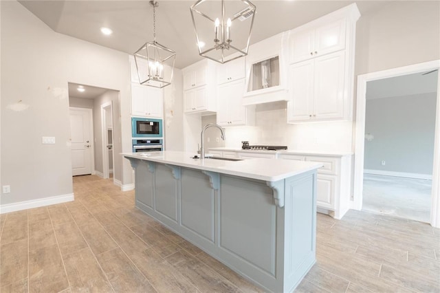 kitchen featuring stainless steel oven, light countertops, built in microwave, a sink, and a notable chandelier