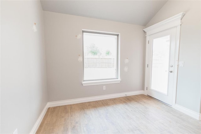 unfurnished room featuring baseboards, light wood finished floors, and vaulted ceiling