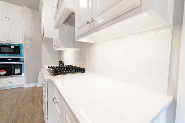 kitchen featuring decorative backsplash, appliances with stainless steel finishes, light wood-type flooring, white cabinets, and under cabinet range hood