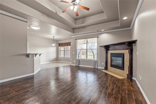 unfurnished living room featuring a raised ceiling, ceiling fan, a fireplace, and dark hardwood / wood-style floors