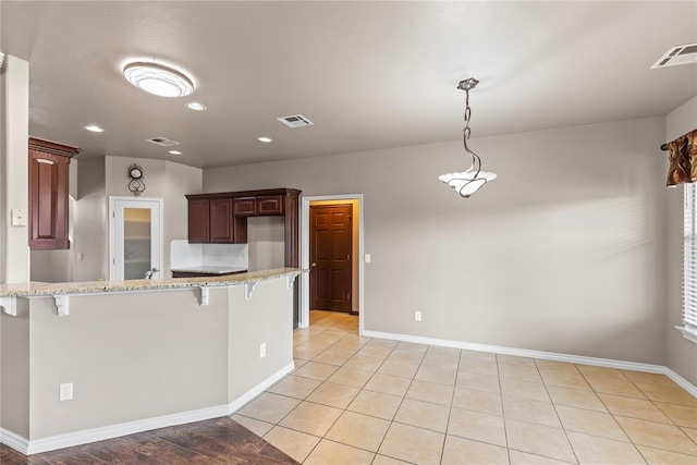 kitchen with light tile patterned floors, light stone counters, decorative light fixtures, a kitchen bar, and kitchen peninsula