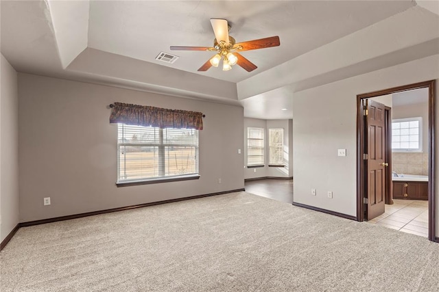 carpeted empty room with a raised ceiling, ceiling fan, and plenty of natural light