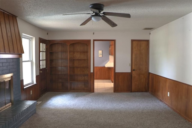 unfurnished living room featuring wood walls, light colored carpet, a fireplace, and a wealth of natural light