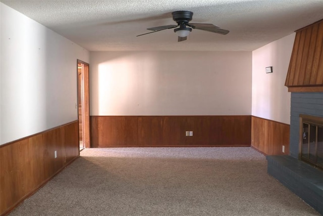 unfurnished living room with ceiling fan, light carpet, a brick fireplace, a textured ceiling, and wooden walls