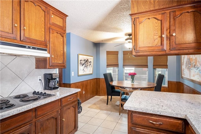 kitchen with wood walls, stainless steel electric stovetop, ceiling fan, light tile patterned floors, and a textured ceiling