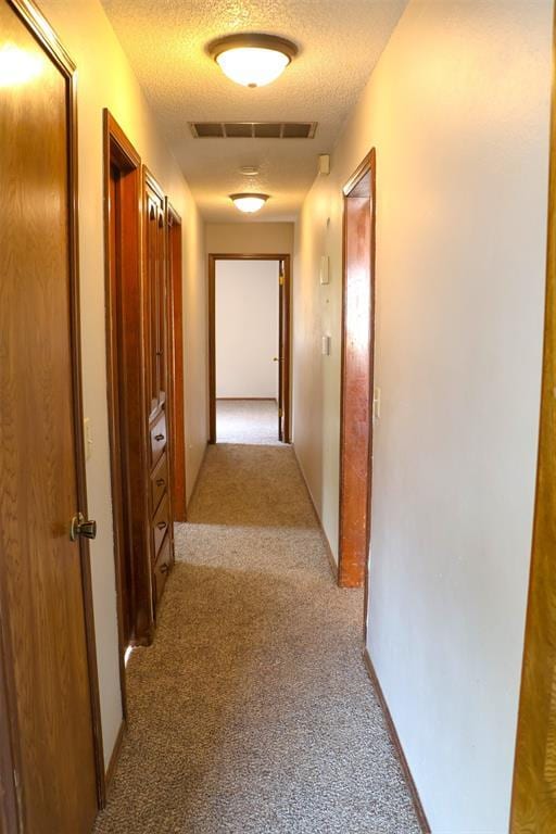 hallway featuring light colored carpet and a textured ceiling