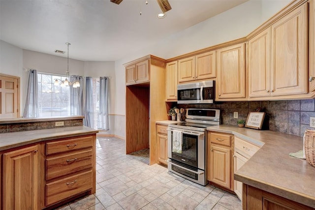 kitchen featuring ceiling fan with notable chandelier, decorative light fixtures, stainless steel appliances, light brown cabinetry, and decorative backsplash