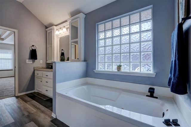 bathroom featuring hardwood / wood-style floors, a tub to relax in, vanity, and vaulted ceiling