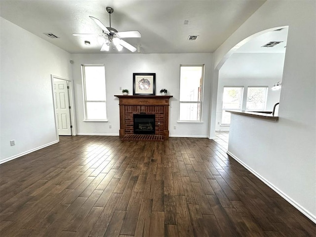 unfurnished living room featuring a brick fireplace, ceiling fan, and dark wood-type flooring