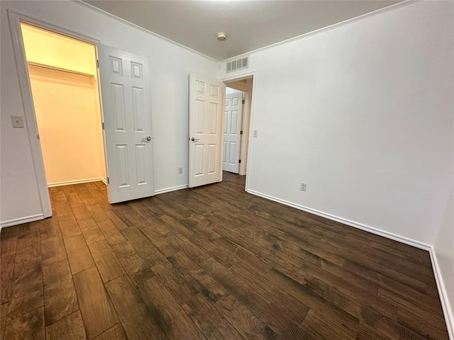 unfurnished bedroom with ornamental molding, a walk in closet, dark wood-type flooring, and a closet