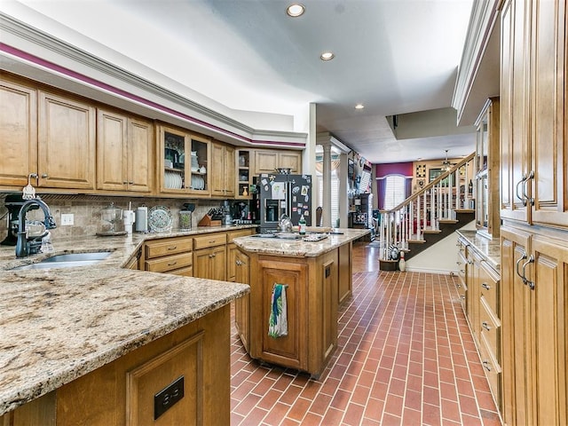 kitchen with sink, decorative backsplash, light stone countertops, refrigerator with ice dispenser, and a kitchen island