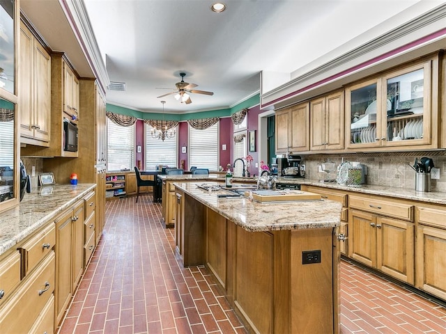 kitchen with pendant lighting, a center island with sink, crown molding, tasteful backsplash, and light stone counters