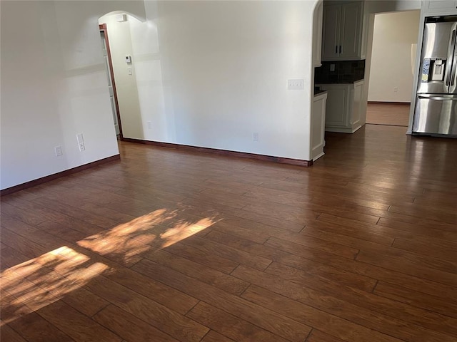 empty room with baseboards, arched walkways, and dark wood-style flooring